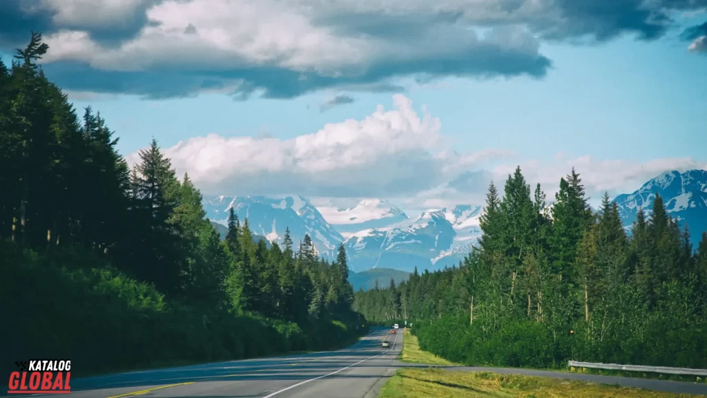 A scenic road surrounded by green forests and snow-capped mountains in Alaska, offering breathtaking views. This beautiful route emphasizes the adventure of exploring the state by answering the question, "Can you drive to Alaska?" with a clear and inviting landscape.